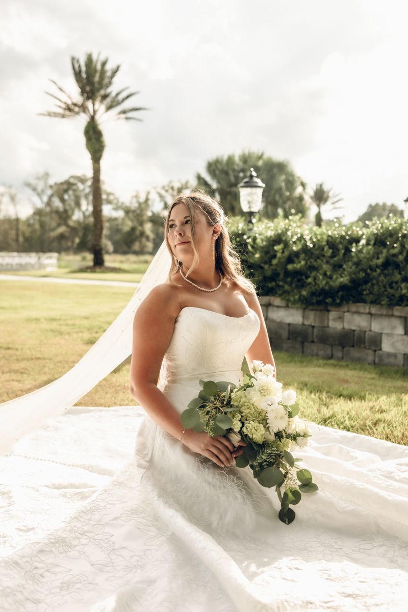 Bride seated with her bouquet under palm trees